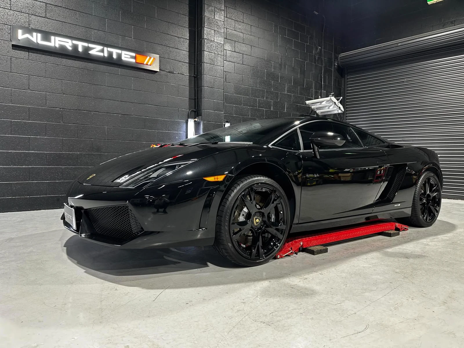 Black Lamborghini Gallardo with reflective paintwork under the Wurtzite sign at Ceramicar Adelaide
