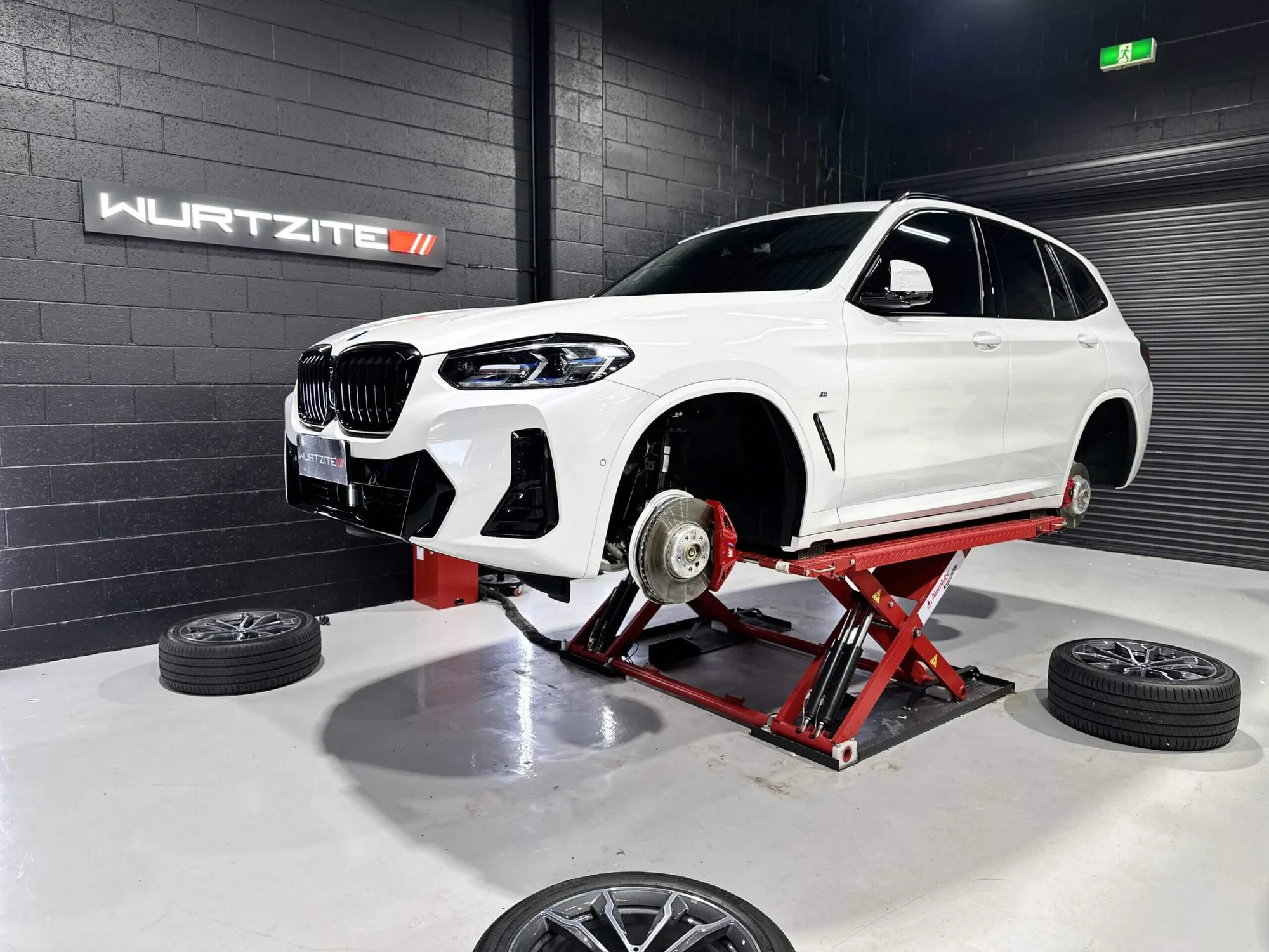 White BMW X3 raised on a jack with all four wheels off for caliper coating