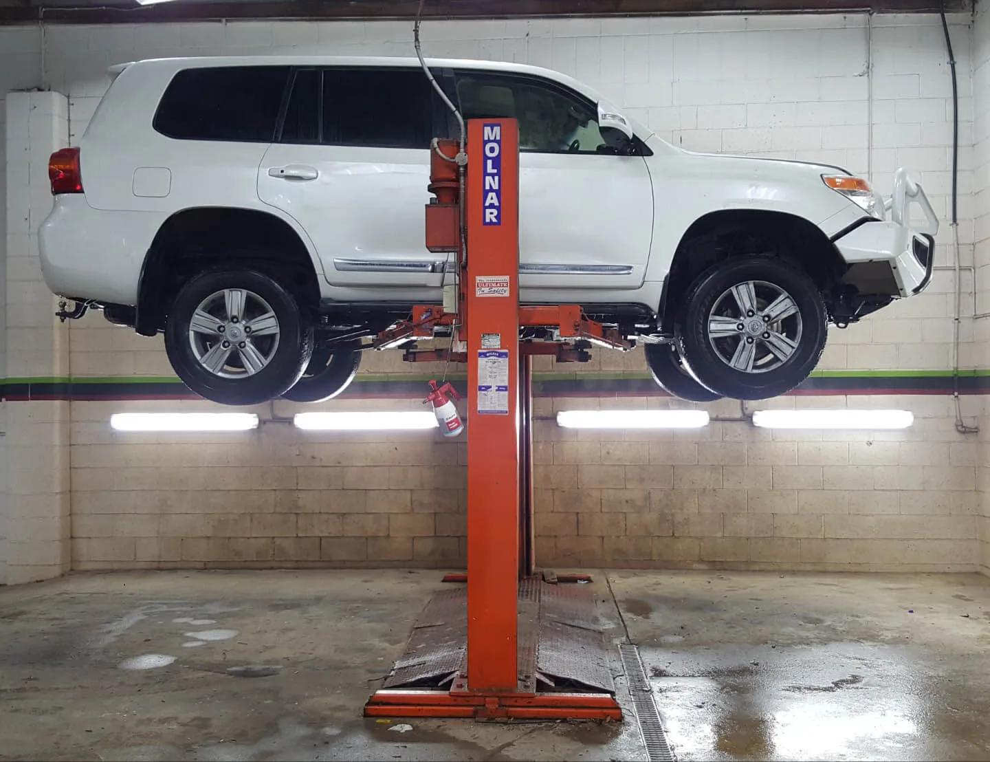 White LandCruiser raised on the two post hoist for an underbody steam clean