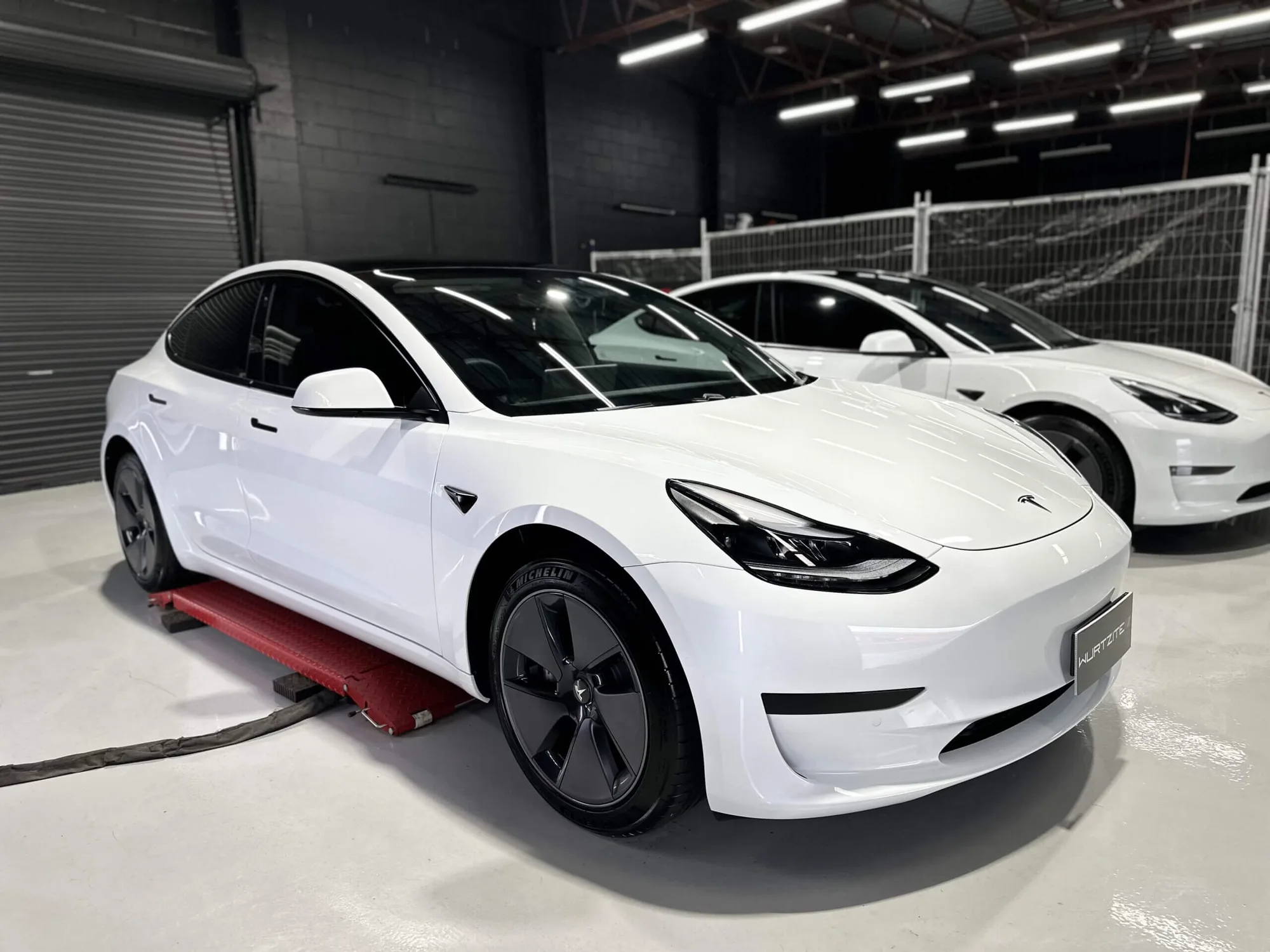 Two white Tesla Model 3s in the workshop waiting on ceramic window tint