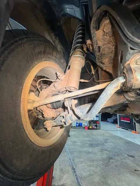 Surface rust and dried mud on a front control arm seen from under the car