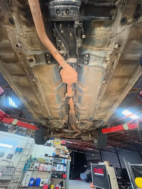 Floorpan and sump of a car on the hoist, thick with road grime before steam cleaning