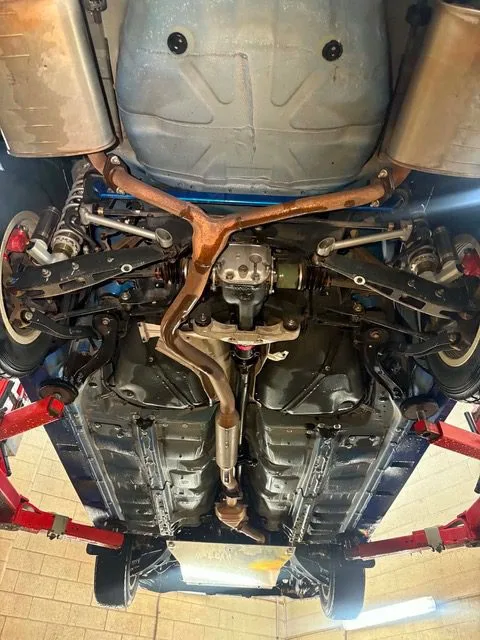 Surface rust across the subframe and exhaust of a car raised for underbody steam cleaning
